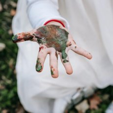 Een meisje dat op het gras zit met verf op haar hand